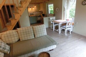 Ein gemütliches Zimmer mit einer Couch, einem Esstisch mit Stühlen, einer Treppe und einer Küchenzeile.