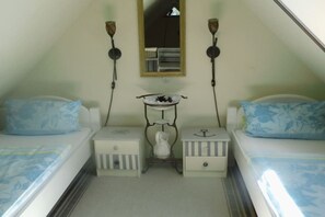 Ein kleiner, dreieckiger Raum mit zwei Betten, einem Nachttisch mit Lampe, einem Spiegel und einem kleinen Regal mit Dekoration.