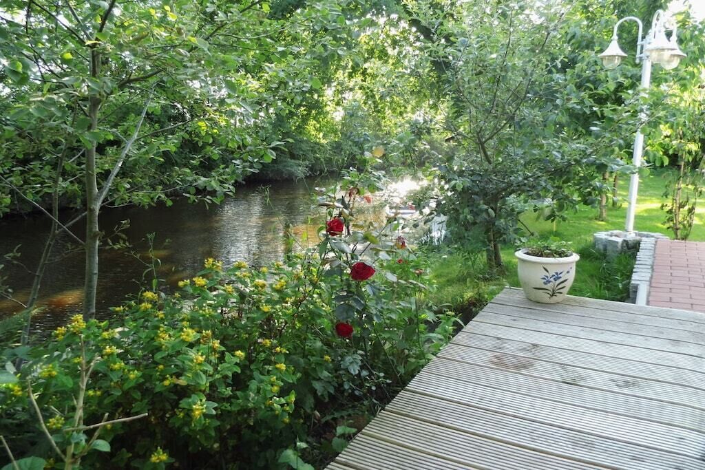 A wooden deck overlooking a river with lush greenery and a potted plant.