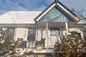 A house with a white exterior, a blue roof, and a porch with two chairs and a table. - Holiday home with 1 bedroom (Neuenkirchen)