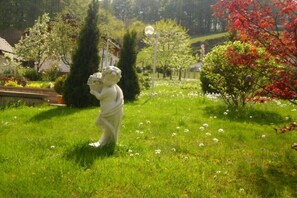 Ein Garten mit einer Statue, Bäumen und blauem Himmel.