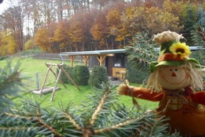 Ein rustikales Blockhaus mit Holzwand und kleiner Veranda, umgeben von einem gepflegten Garten und Bäumen.