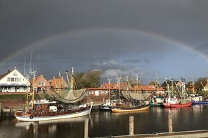 A harbor with fishing boats docked, a rainbow in the sky, and buildings in the background. - Holiday apartment with 1 bedroom (Krummhörn)
