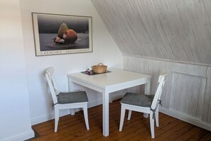 A dining area with a white table and two chairs, a framed photograph on the wall, and a wooden ceiling. - Holiday apartment with 1 bedroom (Krummhörn)