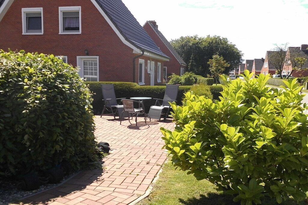 Een bakstenen huis met een betegeld terras, buitenmeubilair en goed onderhouden hagen.
