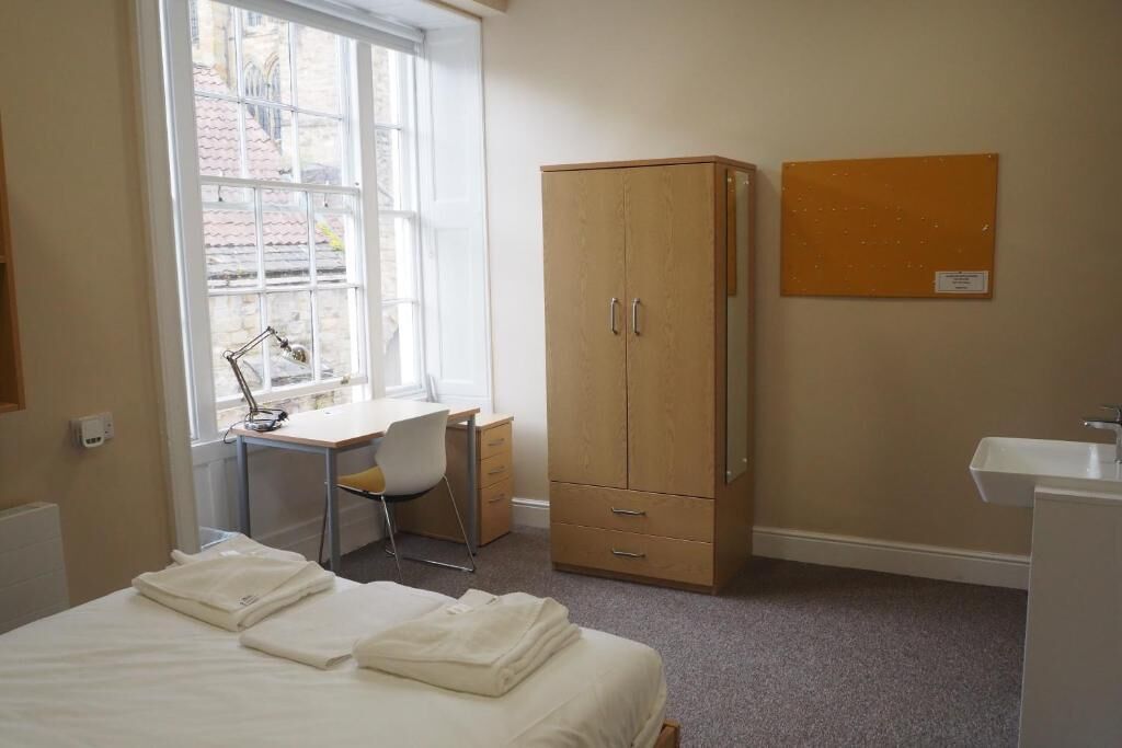 Un dormitorio con cama, escritorio, silla, armario y ventana.