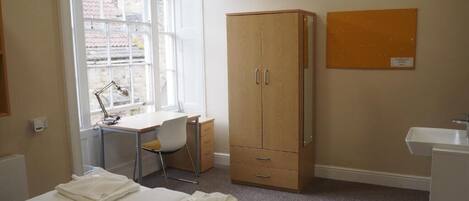 Un dormitorio con cama, escritorio, silla, armario y ventana.