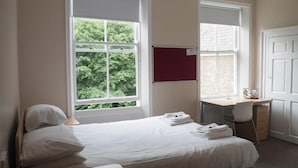 Un dormitorio con cama, escritorio y ventana con vista a árboles.
