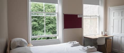 A bedroom with a bed, a desk, and a window with a view of trees.