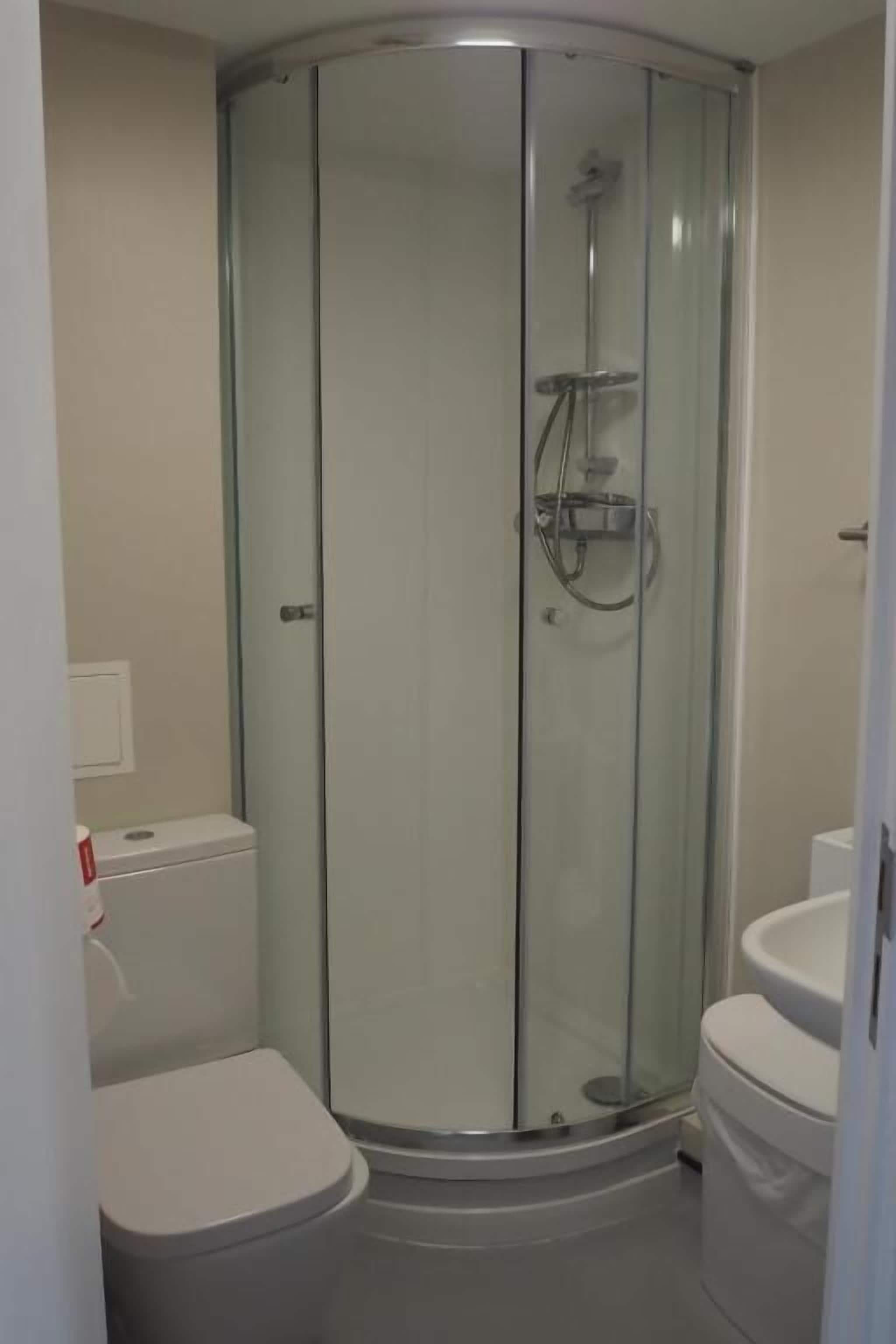 Cabina de ducha con paredes de vidrio, un inodoro y un lavamanos en un baño con rincón.