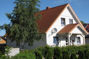 Uma casa de dois andares com telhado de telhas vermelhas, revestimento branco e antena parabólica.