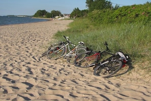 Bicicletas estacionadas numa praia de areia, com água e vegetação ao fundo.
