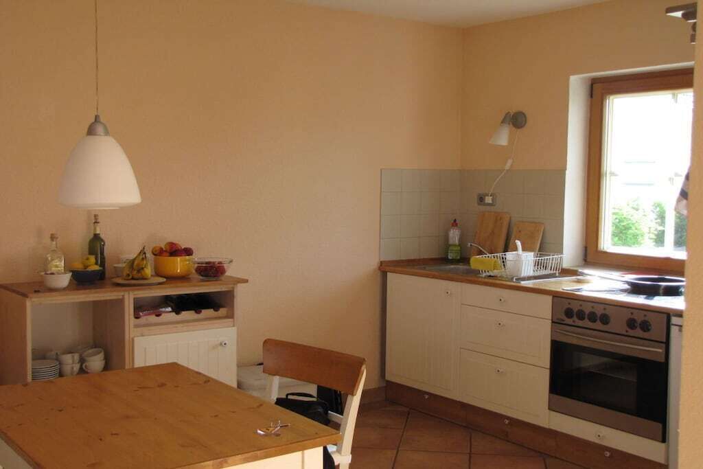 A compact kitchen with a wooden table, a hanging light, a stove, and a window.