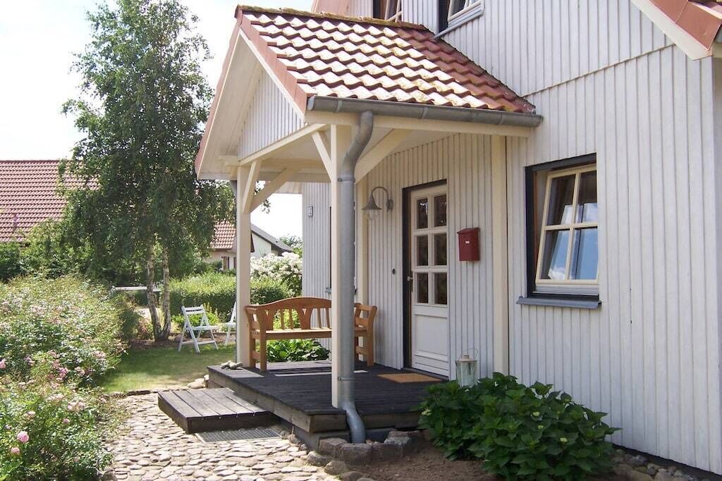 Un bâtiment blanc avec un toit recouvert de tuiles, un banc en bois et un petit espace aménagé en jardin.