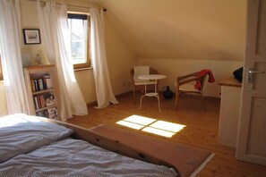 Ein Zimmer mit einem Bett, einem kleinen Tisch, einem Stuhl, einem Bücherregal und einem Fenster mit Vorhängen.