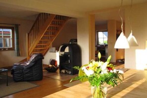 Uma sala de estar com escada de madeira, lareira e mesa de jantar com um vaso de flores.