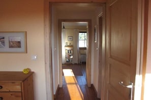 Corredor com piso de madeira que leva a um quarto com cama e janela.