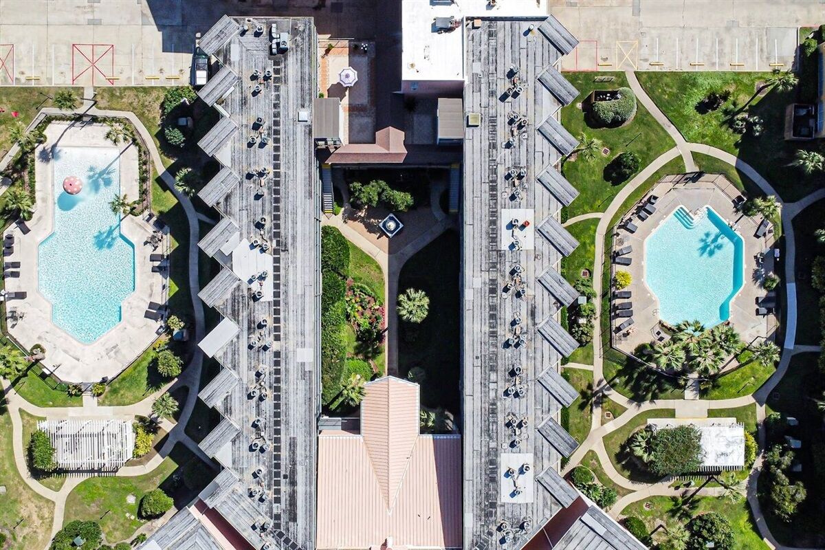 Eine Luftaufnahme eines Hotels mit zwei Schwimmbecken, einem Innenhof und einem Parkplatz.