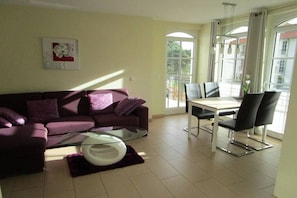 A living room with a sofa, a glass coffee table, a dining area with a table and chairs, and large windows. - House Sea View Apartment A 1.04 (Baabe)