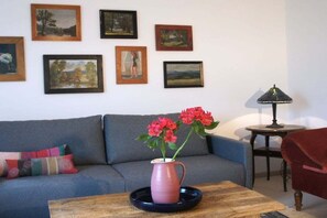 Un salon avec un canapé, une table basse ornée d’un vase de fleurs et des tableaux encadrés accrochés au mur.