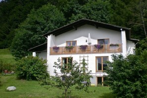 Ein zweistöckiges Gebäude mit Balkon, umgeben von Grün.