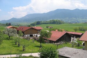 Un paysage rural avec une ferme, des granges et une chaîne de montagnes en arrière-plan.