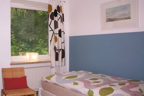 Une chambre à coucher avec un lit, une chaise, une fenêtre avec des rideaux, un radiateur et un tableau encadré au mur.