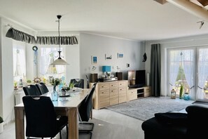 A modern kitchen with a dining area, featuring a large table, chairs, a TV, and a kitchen island. - Holiday home with 2 bedrooms (Greetsiel)