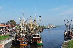 A harbor with several fishing boats docked, a crowd of people on the shore, and a clear sky. - Holiday home with 2 bedrooms (Greetsiel)