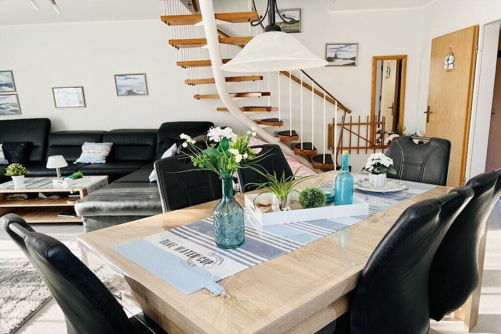 Un salon moderne avec une table à manger en bois, des chaises en cuir noir, un canapé noir et un escalier en colimaçon.