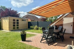 Un patio con una mesa y sillas, un cobertizo de madera y un toldo a rayas.