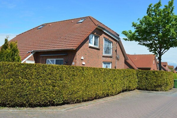 A two-story house with a sloped roof, a brick exterior, and a well-maintained hedge in front. - Holiday home with 2 bedrooms (Greetsiel)