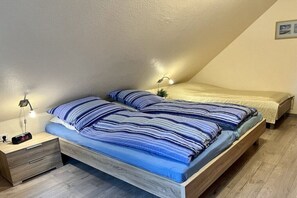 A bedroom with a sloped ceiling, a bed with striped bedding, a bedside table with a lamp, and a clock. - Holiday home with 2 bedrooms (Greetsiel)