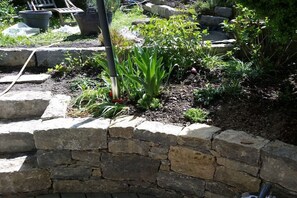Ein Garten mit Steinmauer, verschiedenen Pflanzen und einer hölzernen Bank.