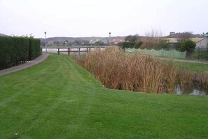 A grassy area with a pond, a pathway, and a fence. - in the Strandslag 103 holiday park in Julianadorp (Julianadorp)