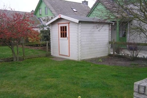 A small, single-story wooden shed with a door and a window, surrounded by a fenced yard. - in the Strandslag 103 holiday park in Julianadorp (Julianadorp)