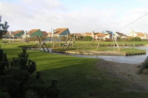Un parc au bord de la rivière, avec des balançoires et un petit pont enjambant l’eau.