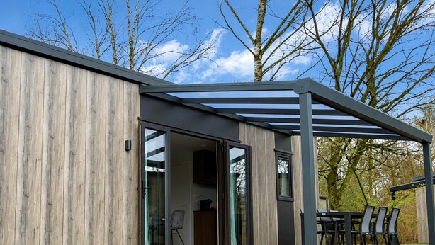 A modern building with a wooden exterior, large glass doors, and a covered outdoor seating area. - Colorado-inspired Cottage for 6 in Slagharen (Slagharen)