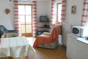 Ein Zimmer mit einer Couch, einem Fernseher auf einem Regal, einer Mikrowelle und einem Tisch mit Tischdecke.
