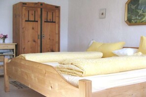 Ein hölzernes Bett mit zwei Kissen und einer Decke, ein Holzschrank, ein Schreibtisch mit Lampe und ein gerahmtes Bild an der Wand.