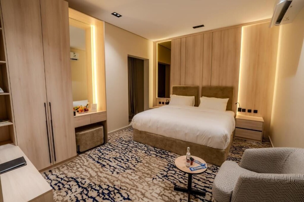 Een hotelkamer met een groot bed, een nachtkastje, een stoel, een kledingkast en een spiegel.