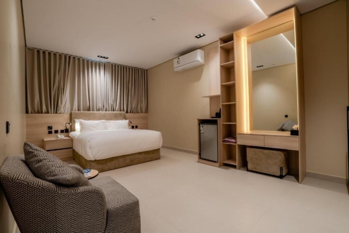 Een moderne hotelkamer met een bed, nachtkastje, kaptafel, spiegel en een klein zithoekje.