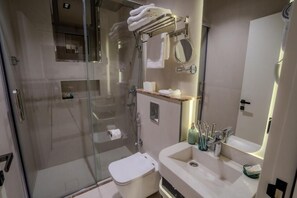Een moderne badkamer met een douche met glazen wand, een wit toilet, een wastafel met spiegel en een handdoekhouder.