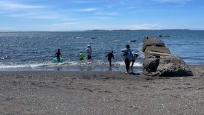 Une plage où l’on voit des gens se promener le long du rivage, un promontoire rocheux et une mer calme.