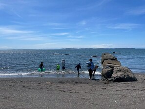 A beach with people walking along the shore, a rocky outcrop, and calm sea. - Surrounded by forests and rivers, this whole-house rental offers a special getaway where you can enjoy camping, barbecues, and bonfires amidst nature. (富津市萩生)