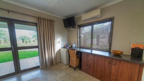A kitchen with a sliding glass door, a small refrigerator, a flat-screen TV mounted above the counter, and a window with blinds.
