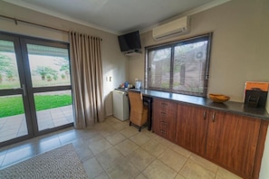 A kitchen with a sliding glass door, a small refrigerator, a flat-screen TV mounted above the counter, and a window with blinds.