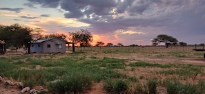 Un paisaje rural con una casa pequeña, campos abiertos y un cielo al atardecer.