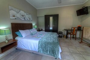 Habitación de hotel con cama, escritorio, silla, televisor y un cuadro en la pared.