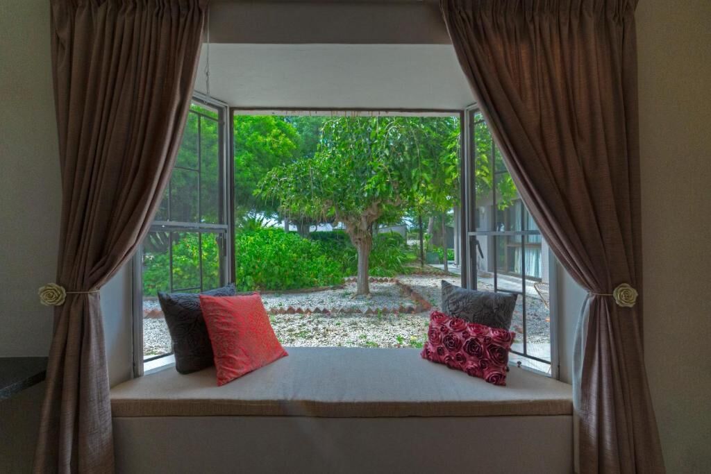 Una habitación con asiento junto a la ventana, vistas de vegetación y un cojín con diseño de rosa.